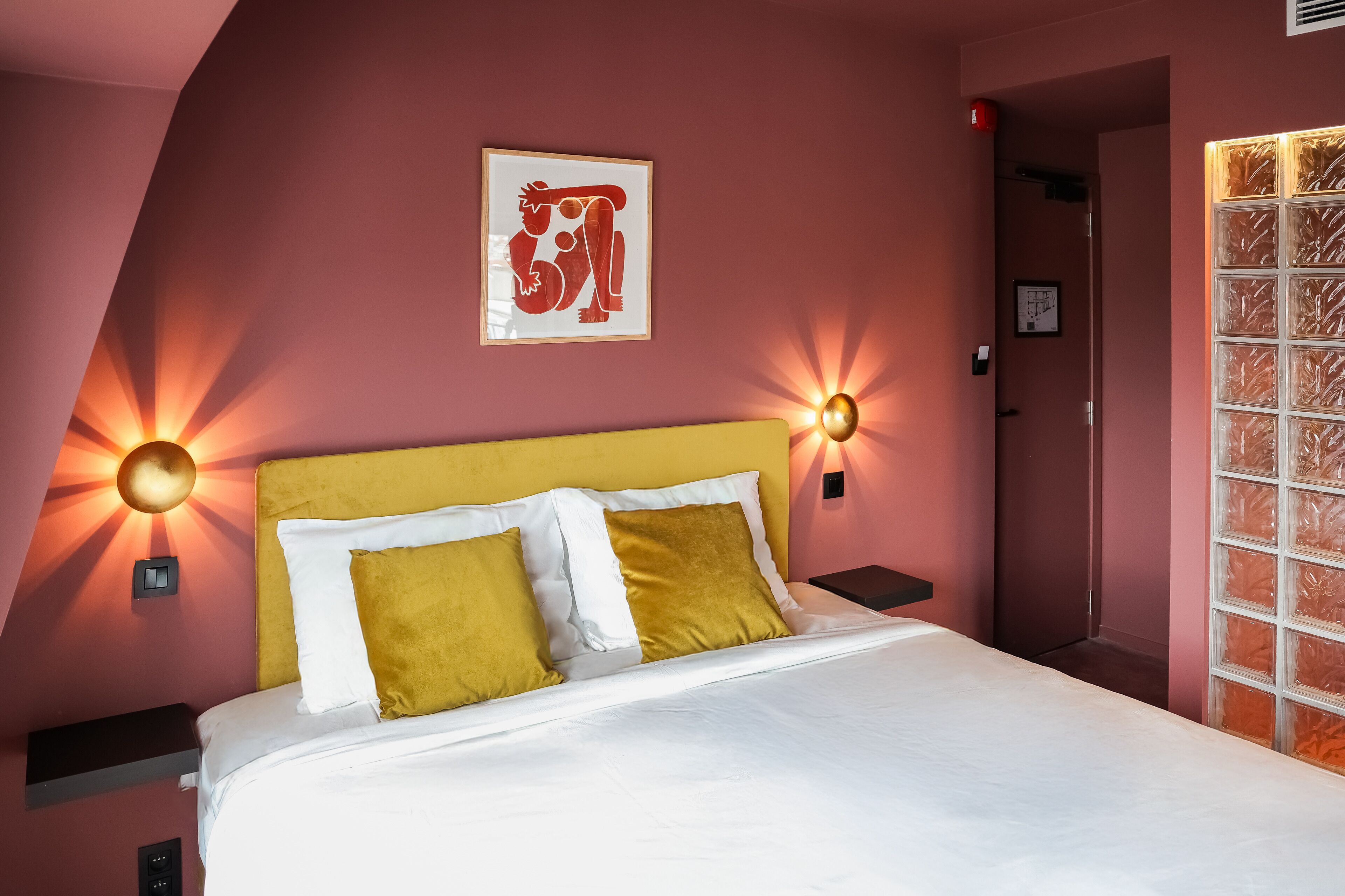 Una cama bien hecha con almohadas blancas y mostaza, un cabecero amarillo y luces fijadas a la pared.