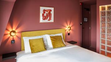 Una cama bien hecha con almohadas blancas y mostaza, un cabecero amarillo y luces fijadas a la pared.