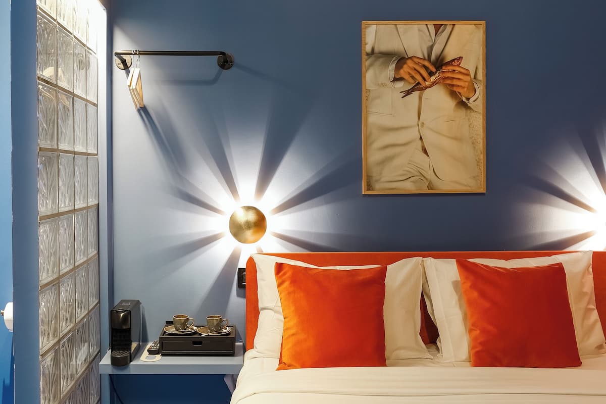 A bedroom with a bed, a nightstand, a wall-mounted lamp, and a framed picture.
