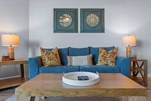 A living room with a blue sofa, two decorative wall pieces, and two lamps on side tables. - TOP FLOOR at The Palms of Destin! (Destin)