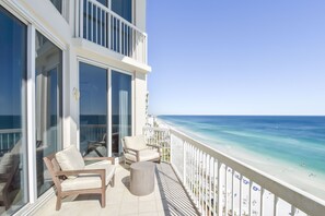 A balcony with a view of the beach, furnished with chairs and a table.