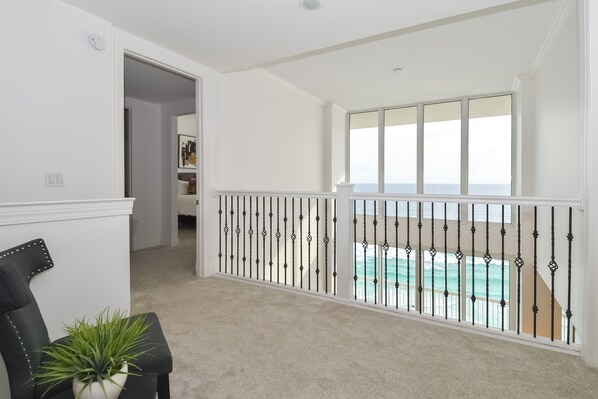 A spacious balcony with a view of the ocean, a white interior, and a potted plant.