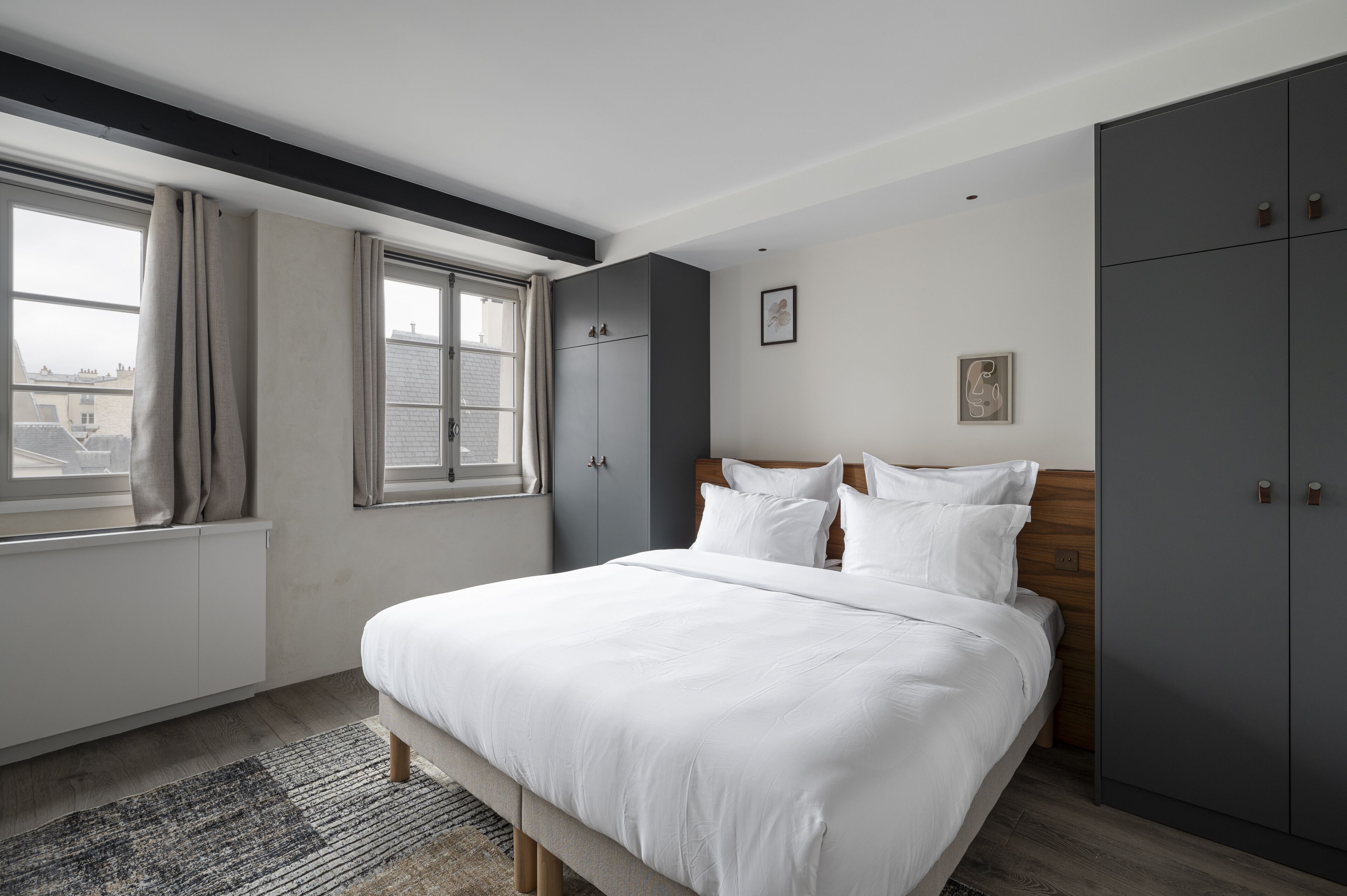 A modern bedroom with a large bed, grey wardrobe, and a window with curtains.