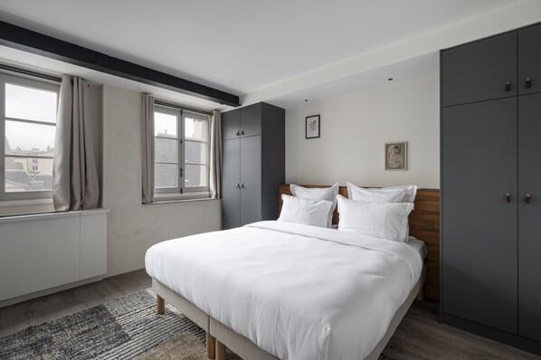 A modern bedroom with a large bed, grey wardrobe, and a window with curtains. - Saint Germain Residence (Paris)
