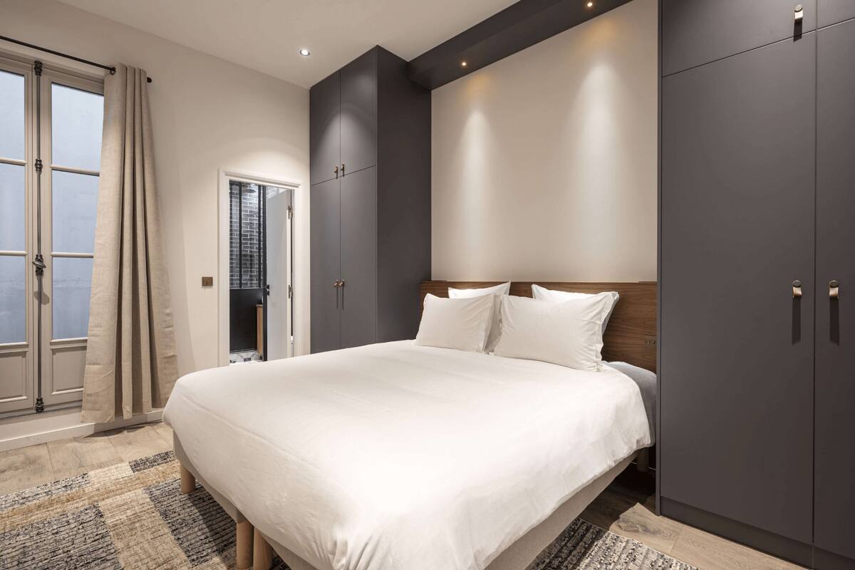 Un dormitorio moderno con una cama grande, armarios oscuros y vistas por la ventana.