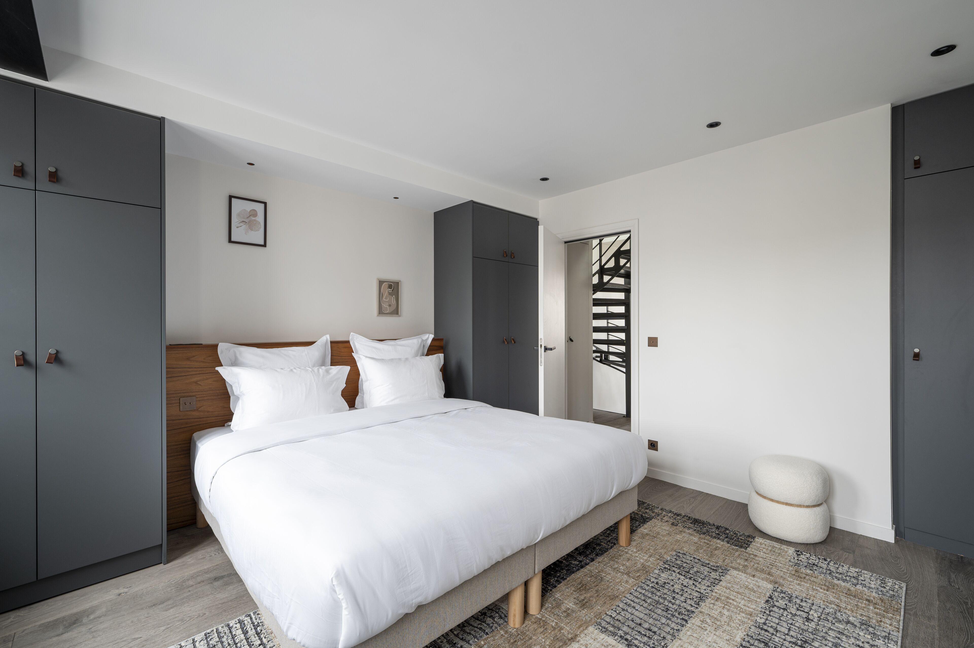 A modern bedroom with a large bed, grey wardrobes, and a staircase.