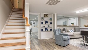 A spacious living area with a wooden staircase, a grey armchair, a beige sofa, and a coffee table. - Moyers Landing - Lakefront Lake Hartwell with Doc (Anderson)