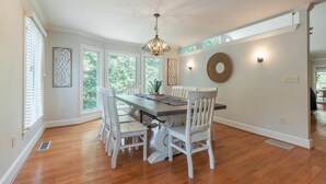 A dining area with a wooden table and white chairs, a chandelier, and decorative wall art. - Moyers Landing - Lakefront Lake Hartwell with Doc (Anderson)