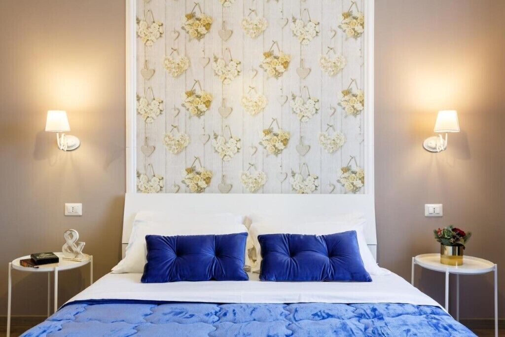 A hotel room with a bed, two bedside tables, a wall with floral wallpaper, and two wall-mounted lamps.