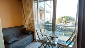 A balcony with a table and chairs, a sofa, and a view of the outside. - T2, parking, 4 personnes, résidence avec piscine (Sète)