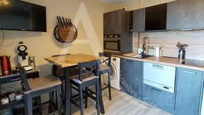 A modern kitchen with a wooden dining table, dark chairs, a built-in oven, and a dishwasher. - T2, parking, 4 personnes, résidence avec piscine (Sète)