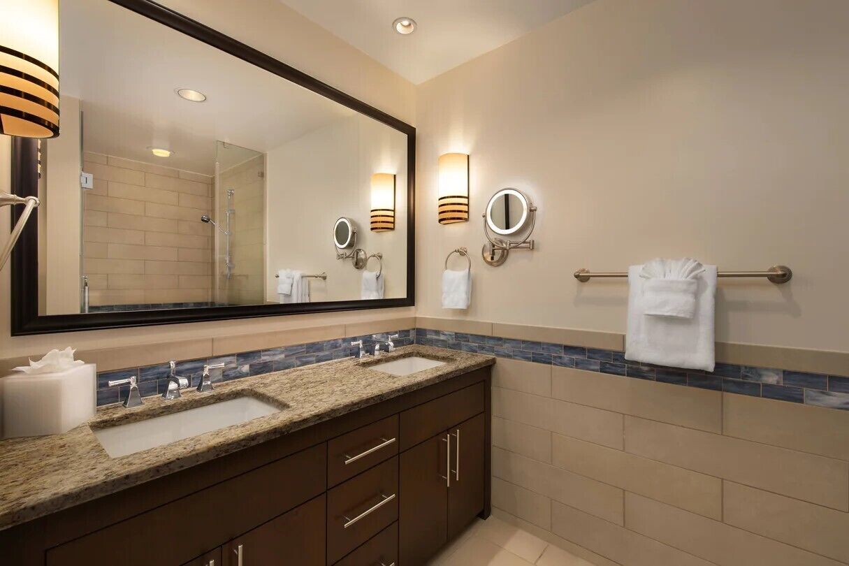 Une salle de bain moderne avec un grand miroir, deux lavabos et des porte-serviettes fixés au mur.