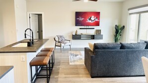 Un salon moderne avec un canapé gris, une table basse en bois et un téléviseur fixé au mur.