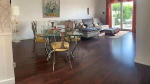 Een woonkamer met een glazen eettafel, een bank en een groot raam met gordijnen.