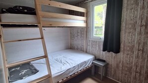 Een slaapkamer met stapelbed, raam, klein tafeltje en gordijn.