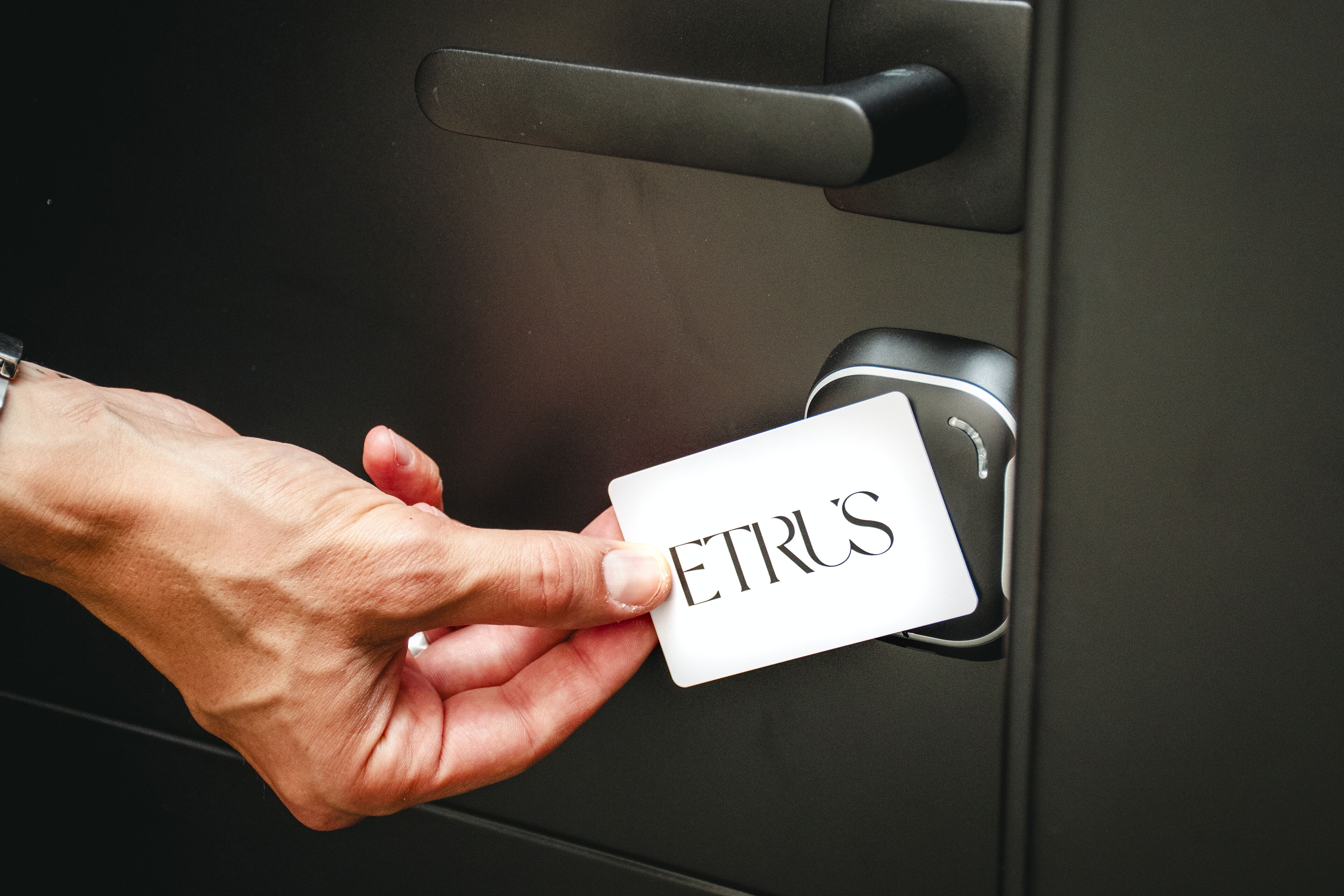 A hand inserting a card labeled "ETRUS" into a door lock.