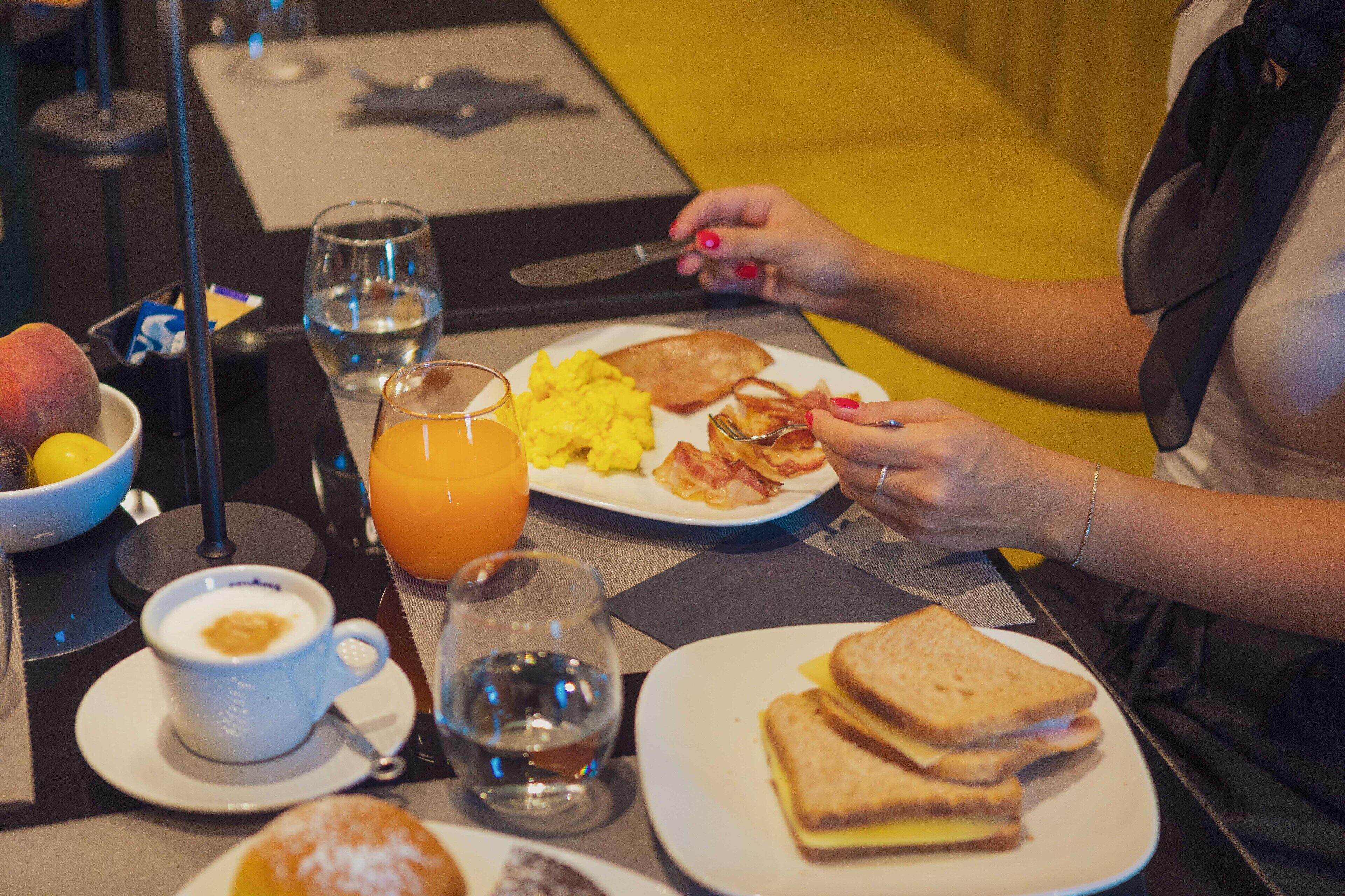 Une table mise pour le petit-déjeuner avec une assiette d’œufs brouillés, des tranches de bacon, des toasts et un verre de jus d’orange.