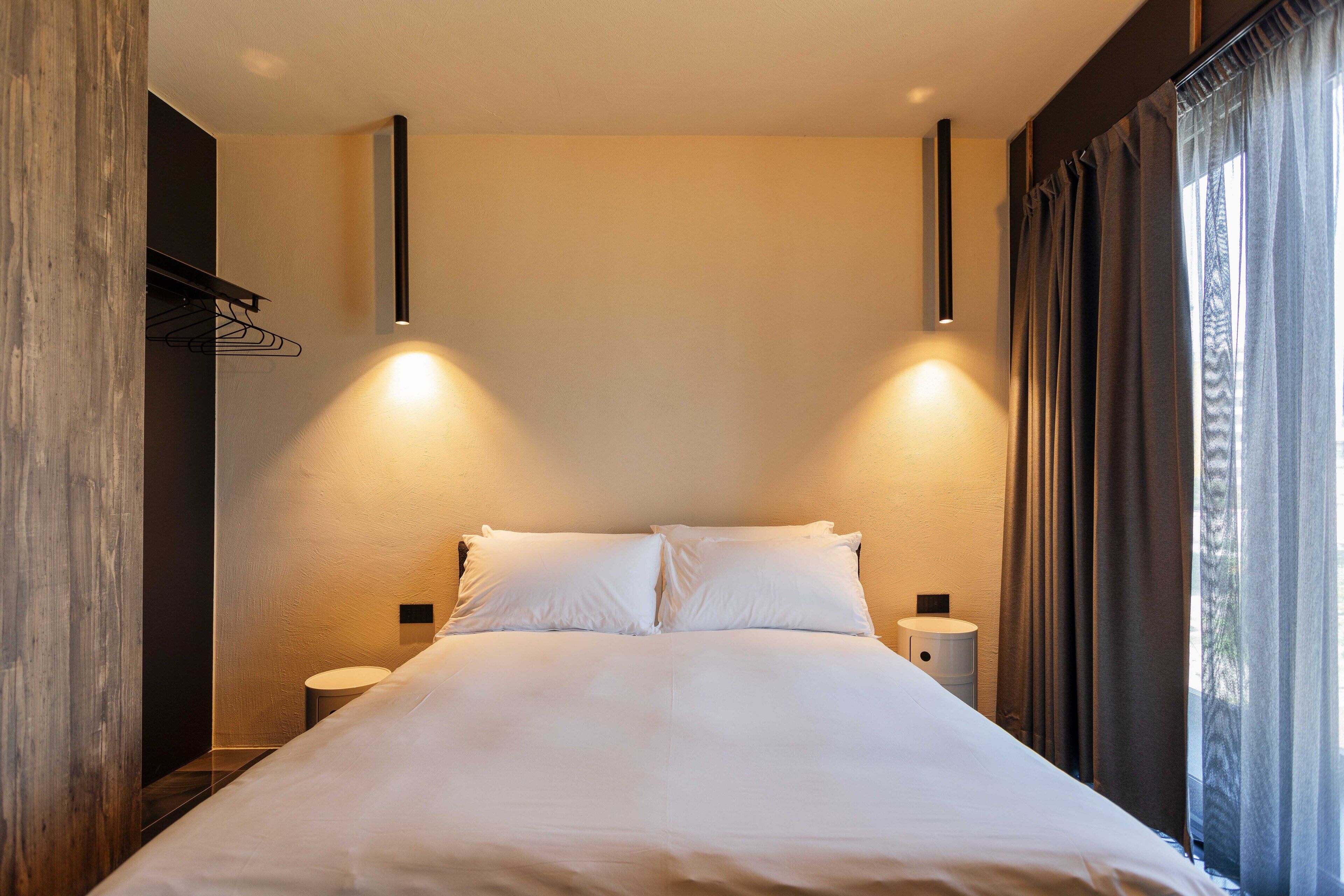 Ein modernes Hotelzimmer mit einem großen Bett, zwei Nachttischen und einem fensterbelaubten Fenster.