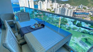Un balcon doté de meubles en osier et offrant une vue sur le paysage urbain et les montagnes.