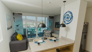 Une cuisine moderne dotée d’un grand îlot central, d’un coin repas avec un canapé et des chaises, et offrant une vue sur la ville grâce à de grandes fenêtres.