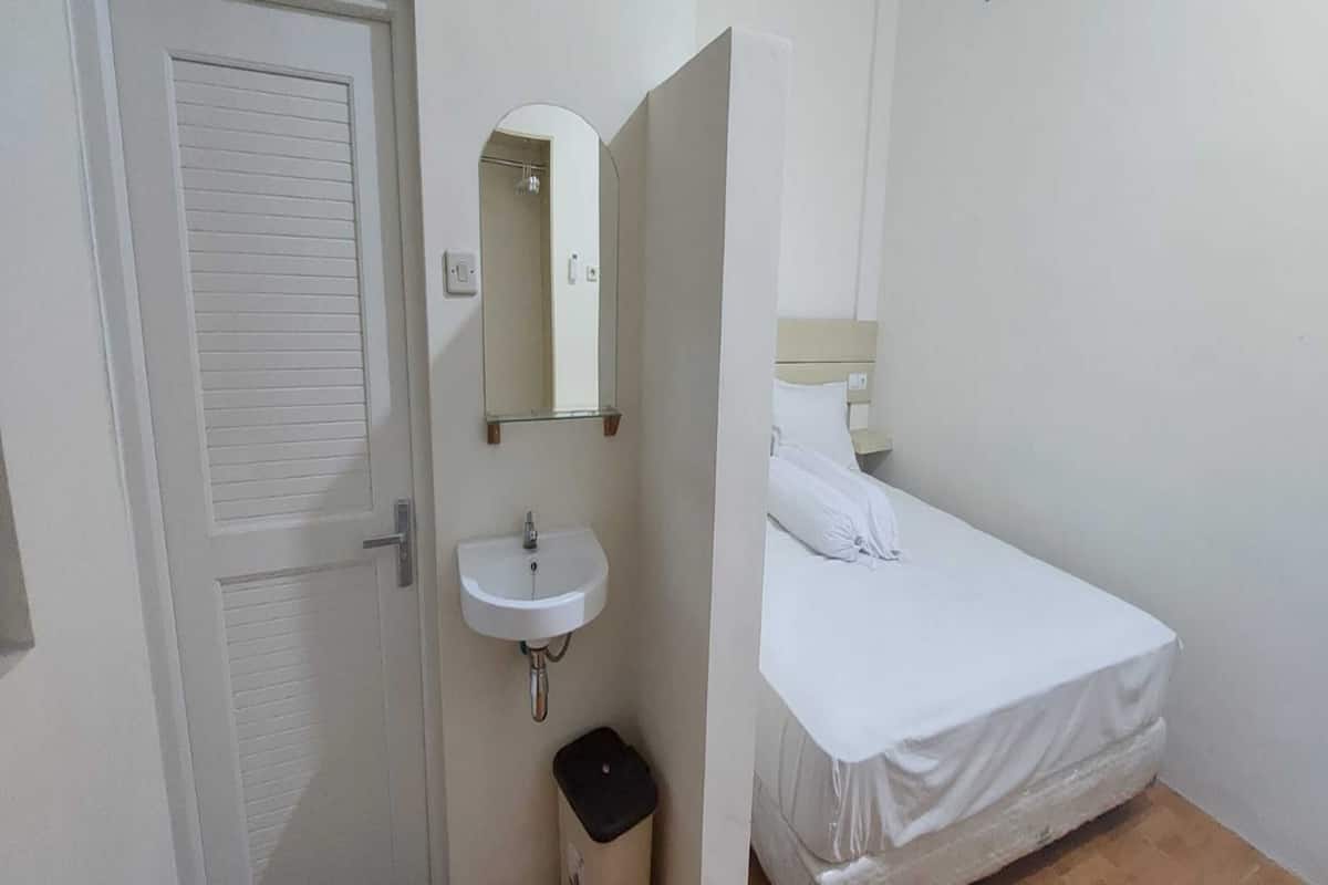 Une petite chambre avec un lit simple, un lavabo blanc et un miroir au-dessus.