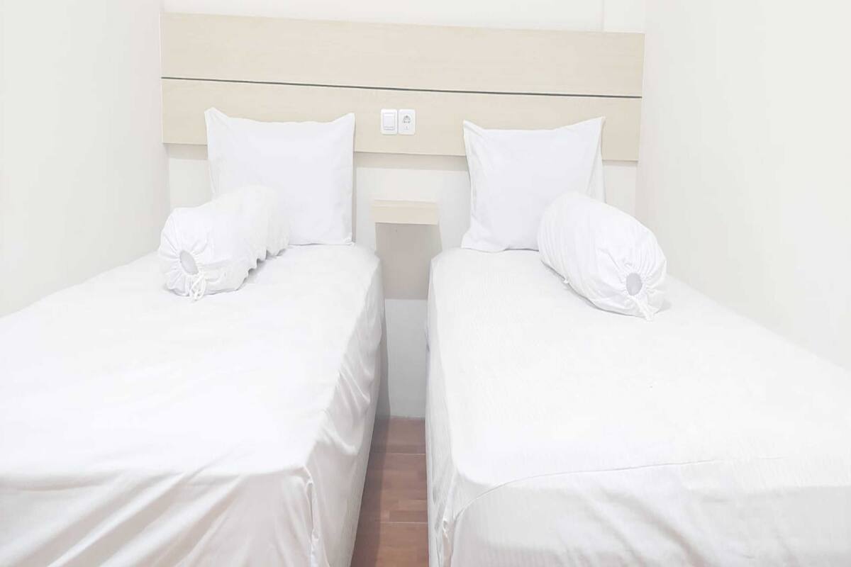 Deux lits simples avec du linge de lit blanc et des têtes de lit, une tête de lit en bois et un mur de couleur claire.