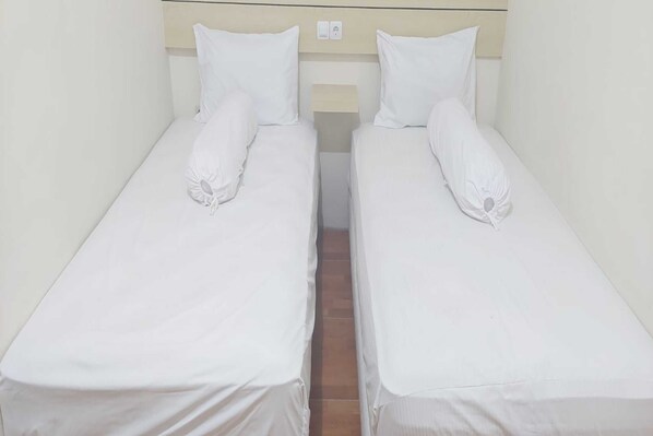Dos camas individuales con sábanas y almohadas blancas, un cabecero de madera y una mesita de noche con interruptor de luz.