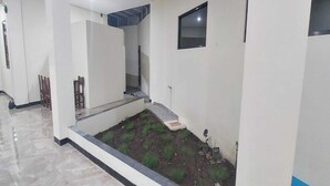 A hallway with a tiled floor, a small garden area with grass and rocks, and a window on the wall. - Capital O 93489 An Nur Homestay Syariah (Mungkid)