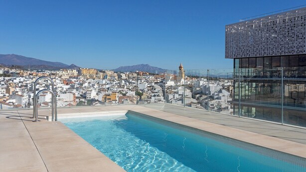 Une piscine sur le toit offrant une vue panoramique sur la ville, avec une tour imposante et des montagnes en arrière-plan.