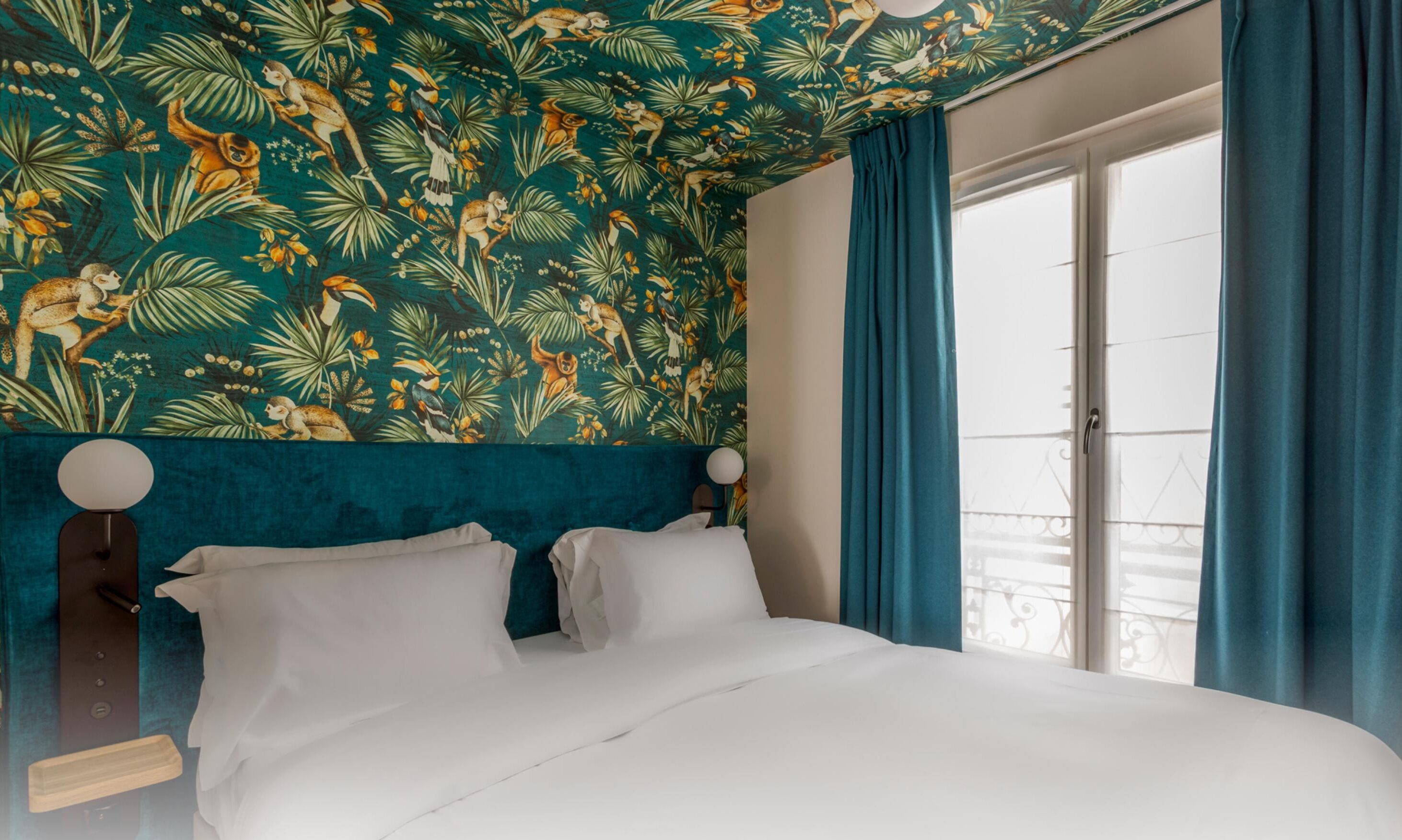 A bed with white linens, teal curtains, and a tropical-themed wall.