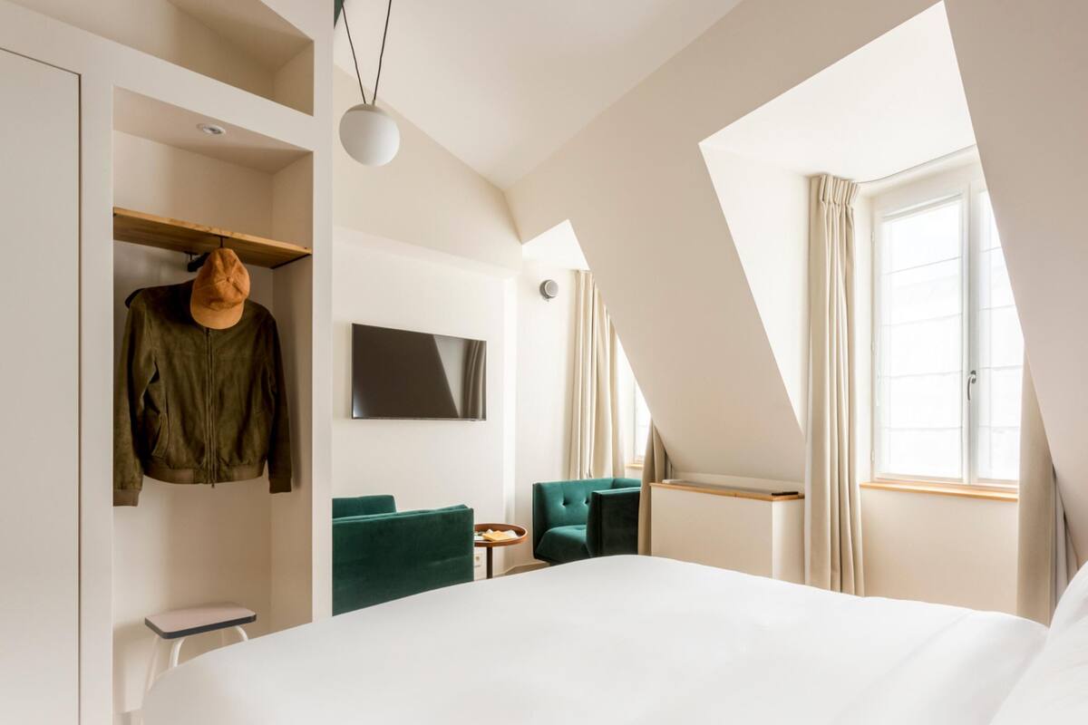 A modern hotel room with a large bed, a TV, a green chair, and a wardrobe.