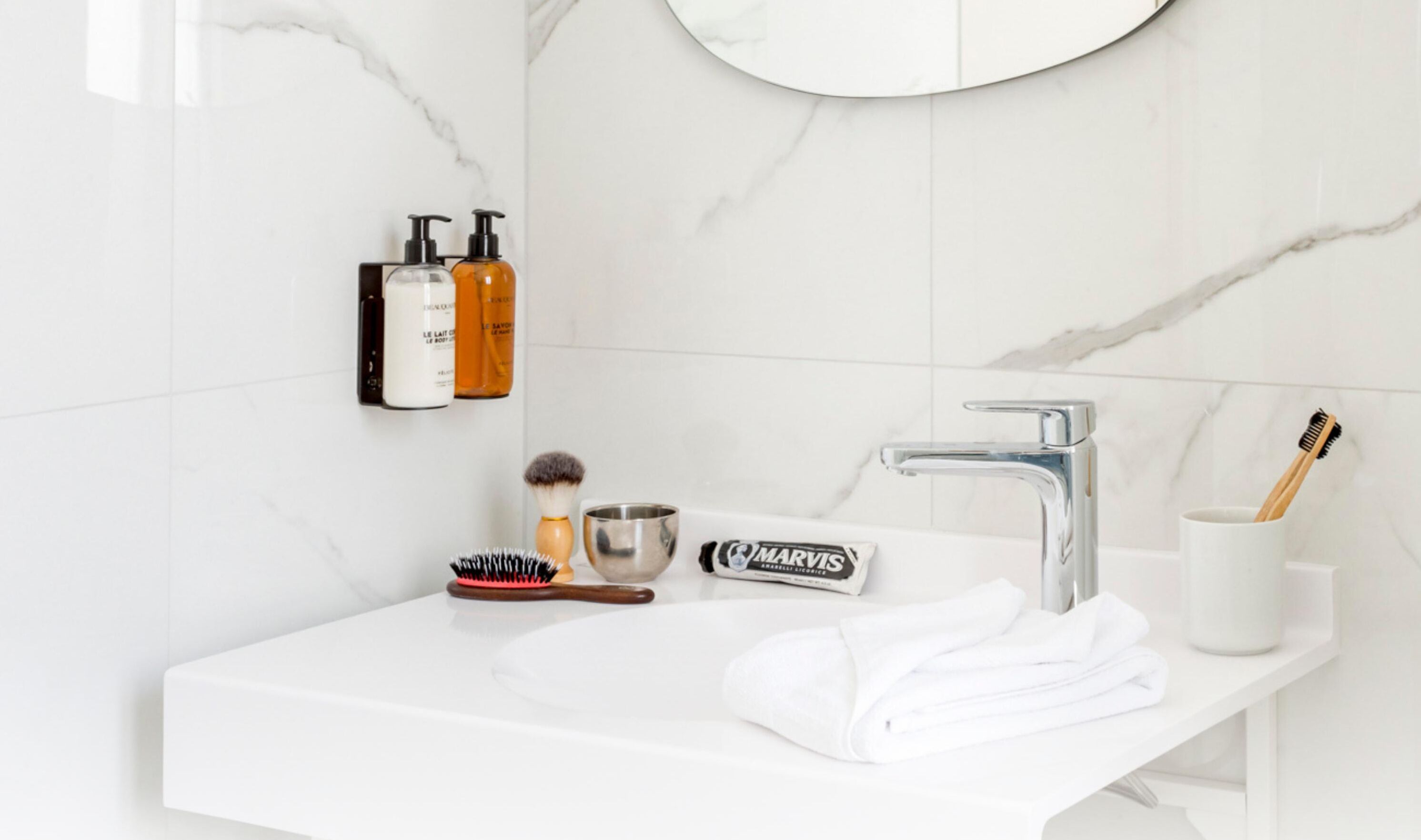 Ein Badezimmer mit einem weißen Waschbecken, einem Spiegel und Toilettenartikeln, darunter eine Zahnbürste, ein Rasierer und eine Haarbürste.