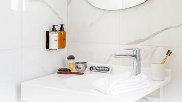 Ein Badezimmer mit einem weißen Waschbecken, einem Spiegel und Toilettenartikeln, darunter eine Zahnbürste, ein Rasierer und eine Haarbürste.
