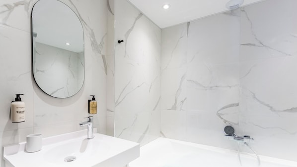 Un baño moderno con lavamanos de mármol blanco, un espejo grande y una zona de ducha.