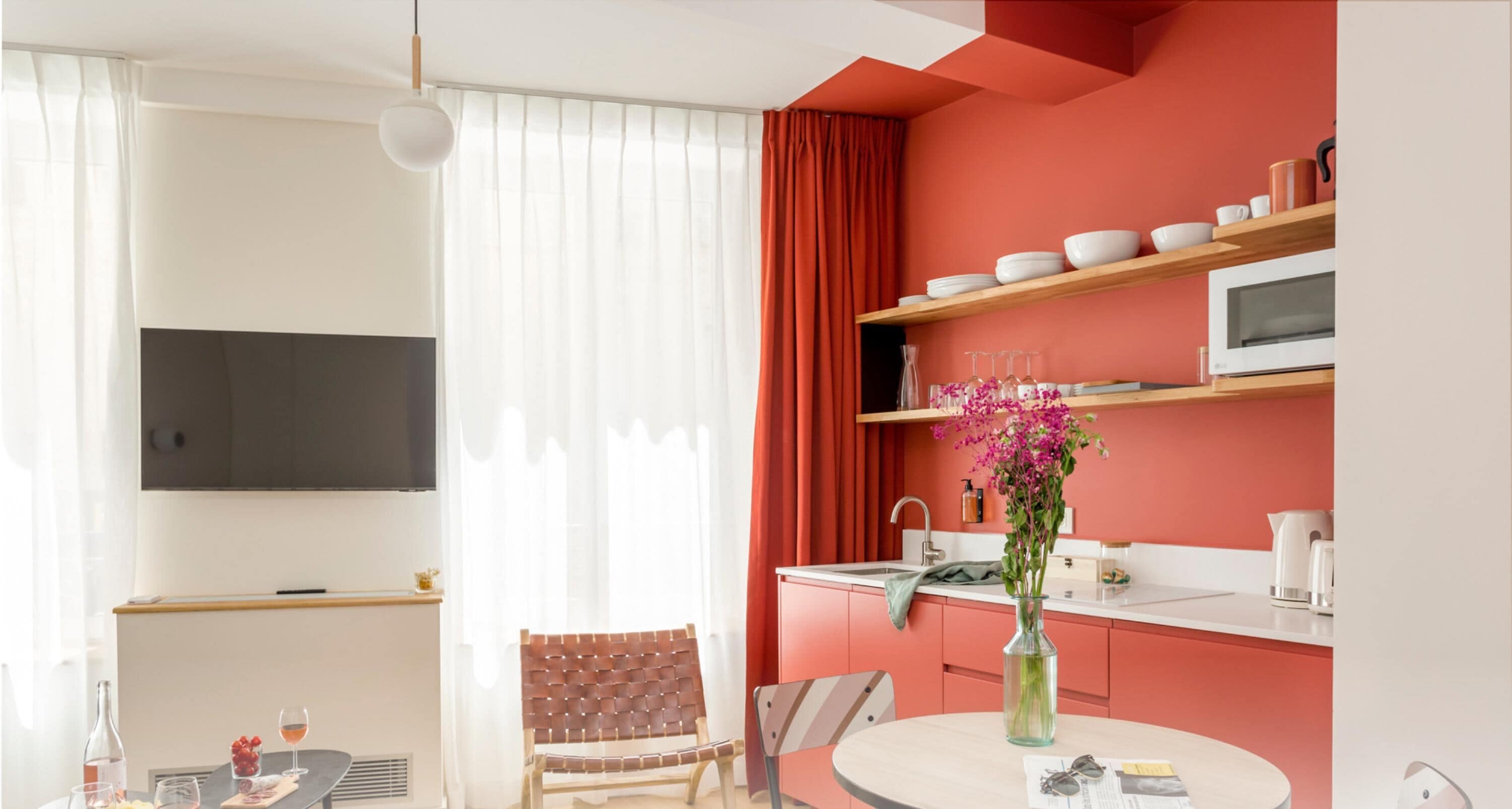 A modern kitchen with white countertops, a microwave, and a red accent wall.