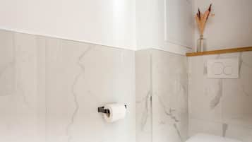 Un baño con paredes de mármol, un dispensador de papel higiénico y un jarrón decorativo con plantas secas.