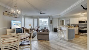 Un vaste espace de vie comprenant un grand téléviseur, une table à manger avec des chaises, un canapé et un lustre.
