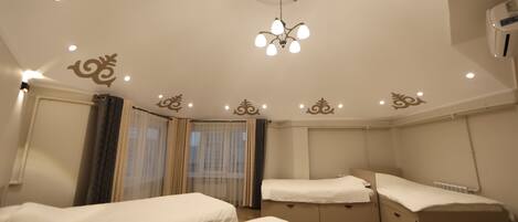 A hotel room with two single beds, a ceiling fan, a chandelier, and decorative wall patterns.