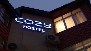 Een hostelbord met de naam 'Cozy Hostel' verlicht tegen een donkere lucht.