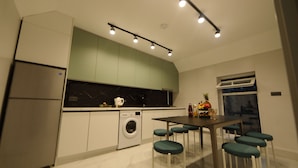 Een moderne keuken met een ingebouwde wasmachine, een eethoek met barstoelen en een groot raam.