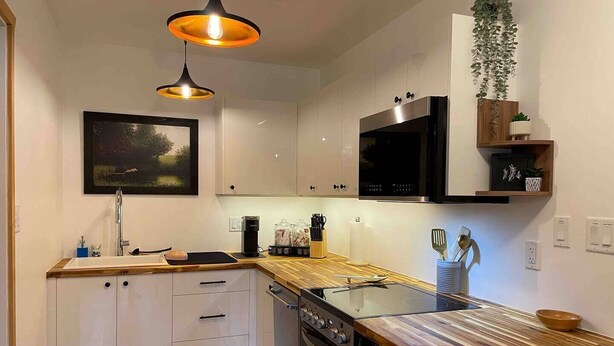 A modern kitchen with white cabinets, a wooden countertop, a built-in oven, a microwave, and a hanging plant. - Su Casa Suite with Sauna (Salmo)