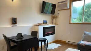 A modern living room with a flat-screen TV mounted on the wall, a dining table with chairs, a sofa, and a small ottoman. - Su Casa Suite with Sauna (Salmo)