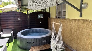 A hot tub with a wooden bench, surrounded by a bamboo fence, and a hanging macrame swing. - Tartane Beach SPA 2 MER (La Trinité)