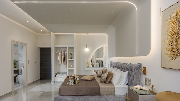 Un dormitorio moderno con una cama grande, mesitas de noche, un armario y un baño a la vista al fondo.