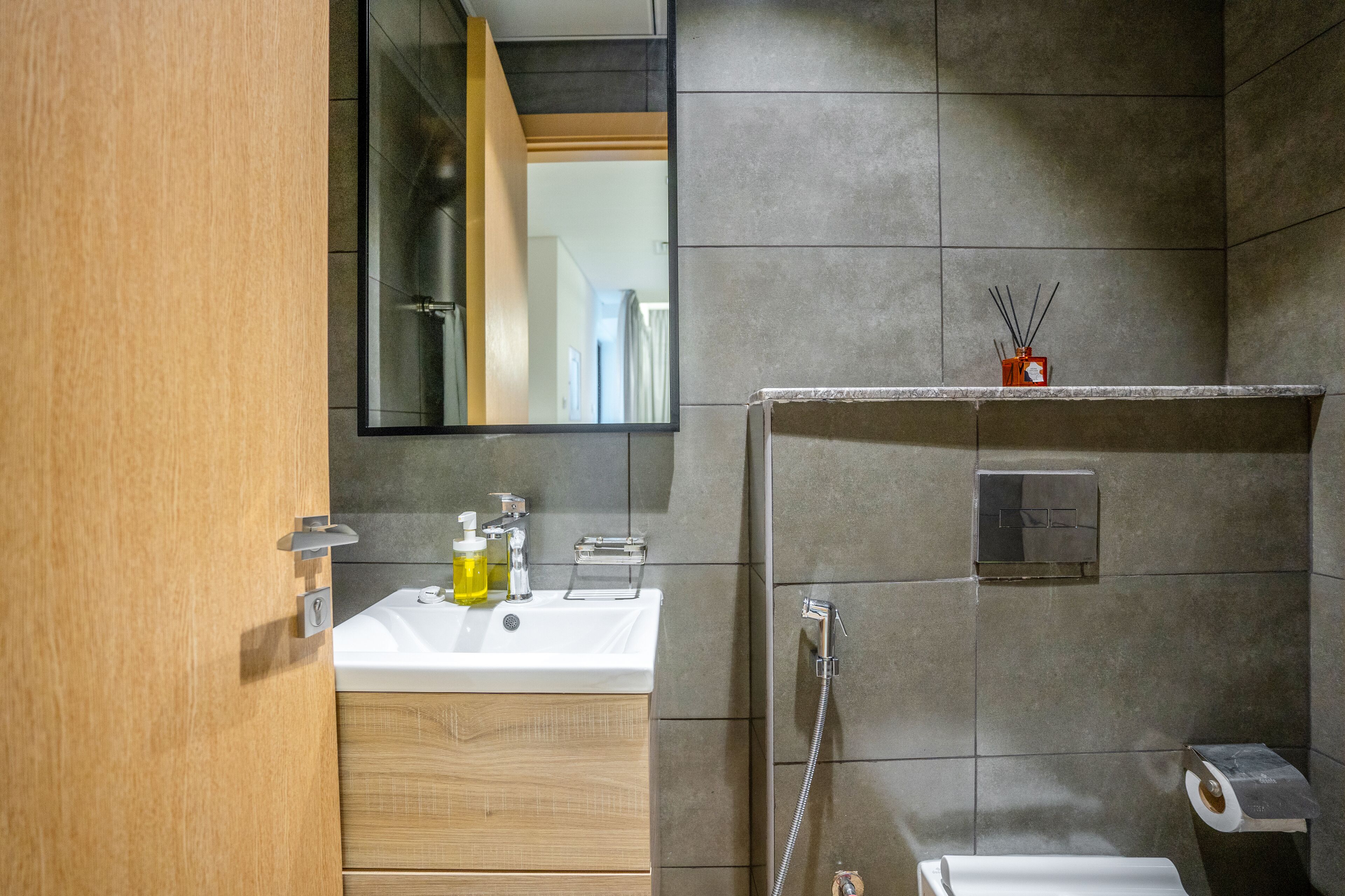 A modern bathroom with a wooden vanity, a mirror, a sink, a shower, and a toilet.