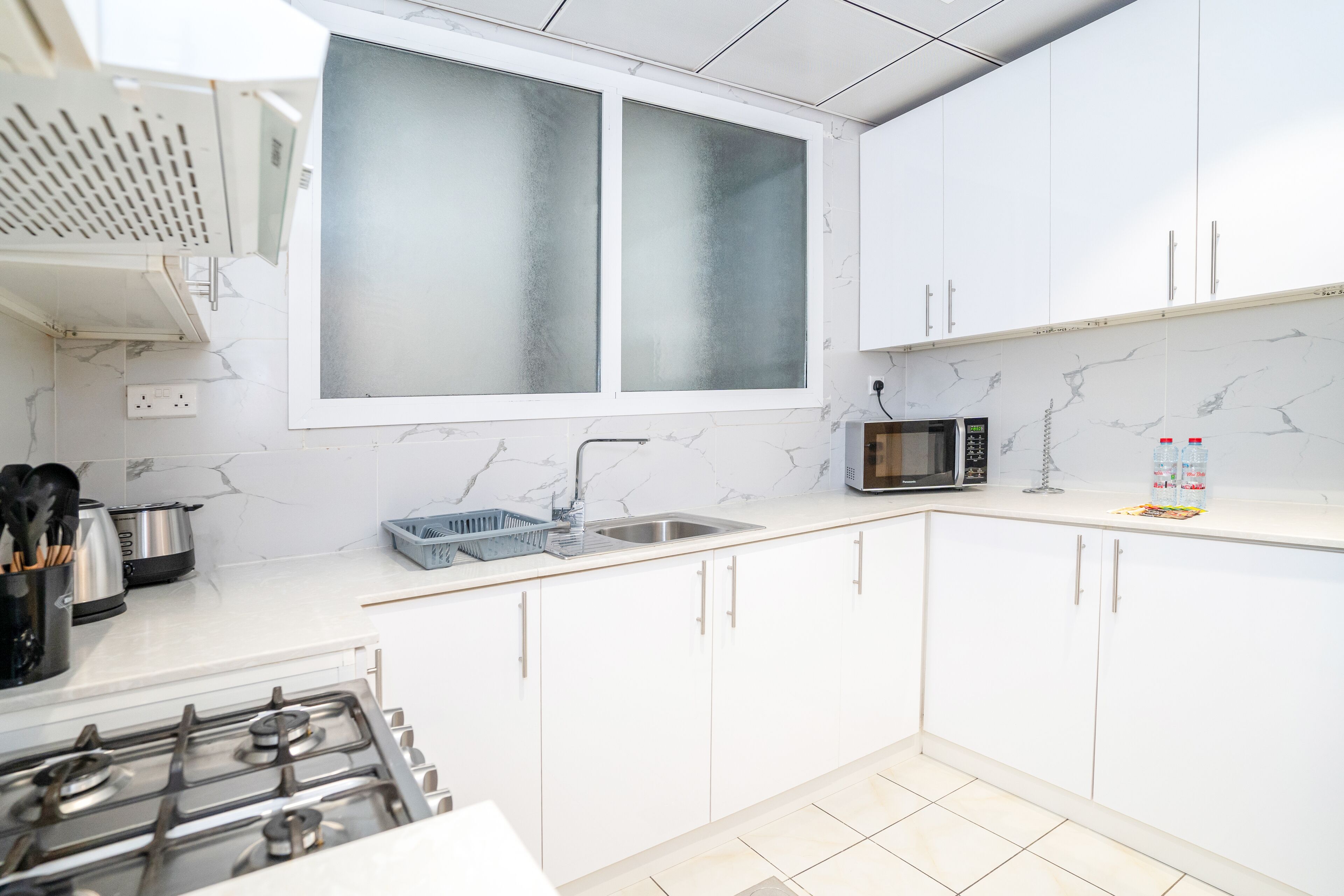 Une cuisine moderne avec des meubles blancs, un évier en acier inoxydable, un four à micro-ondes et une cuisinière à gaz.