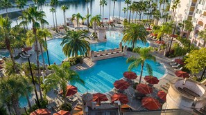 Ein Resort-Poolbereich mit mehreren Schwimmbecken, Palmen und Liegestühlen.
