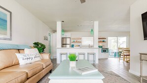 Ein modernes Wohnzimmer mit einem beigen Sofa, einem Glastisch und Blick in die Küche.