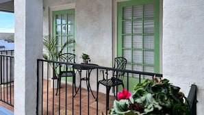 A balcony with a table and chairs, green-framed windows, and potted plants.
