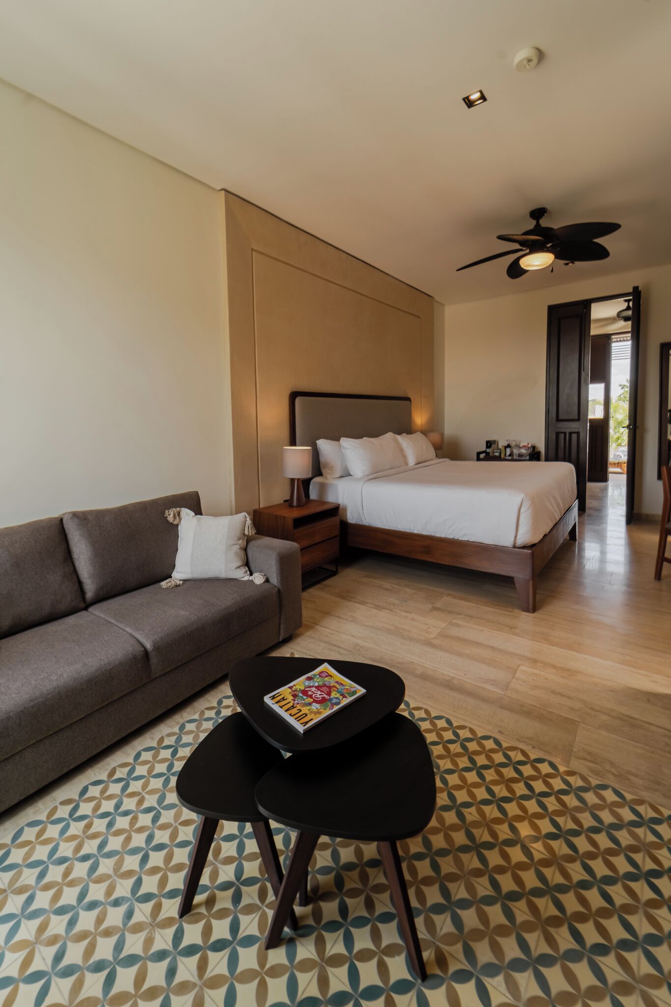 Quarto de hotel moderno com cama, sofá, mesa pequena e ventilador de teto.